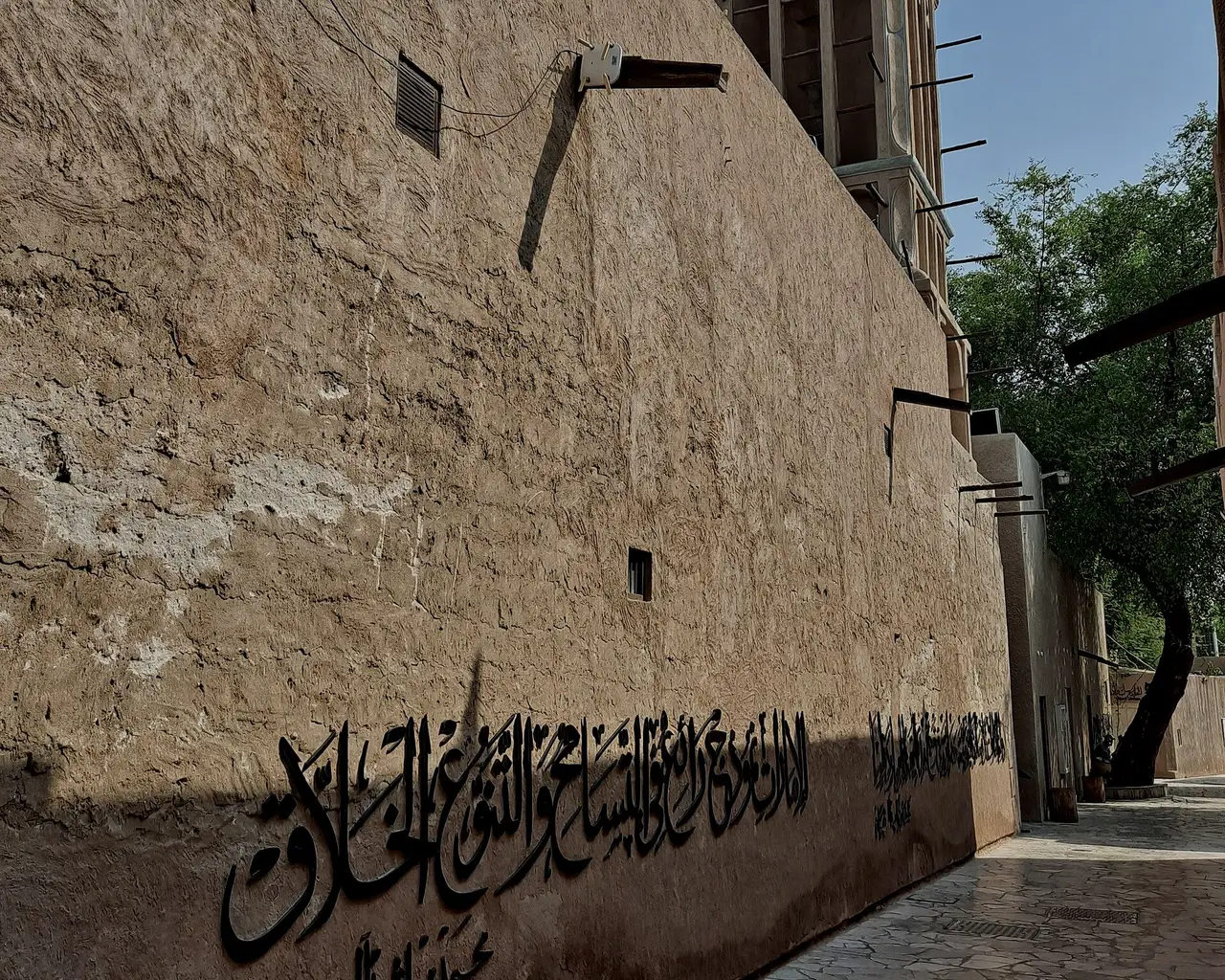 Sunlit plaster wall in Al Fahidi, Dubai, with Arabic calligraphy